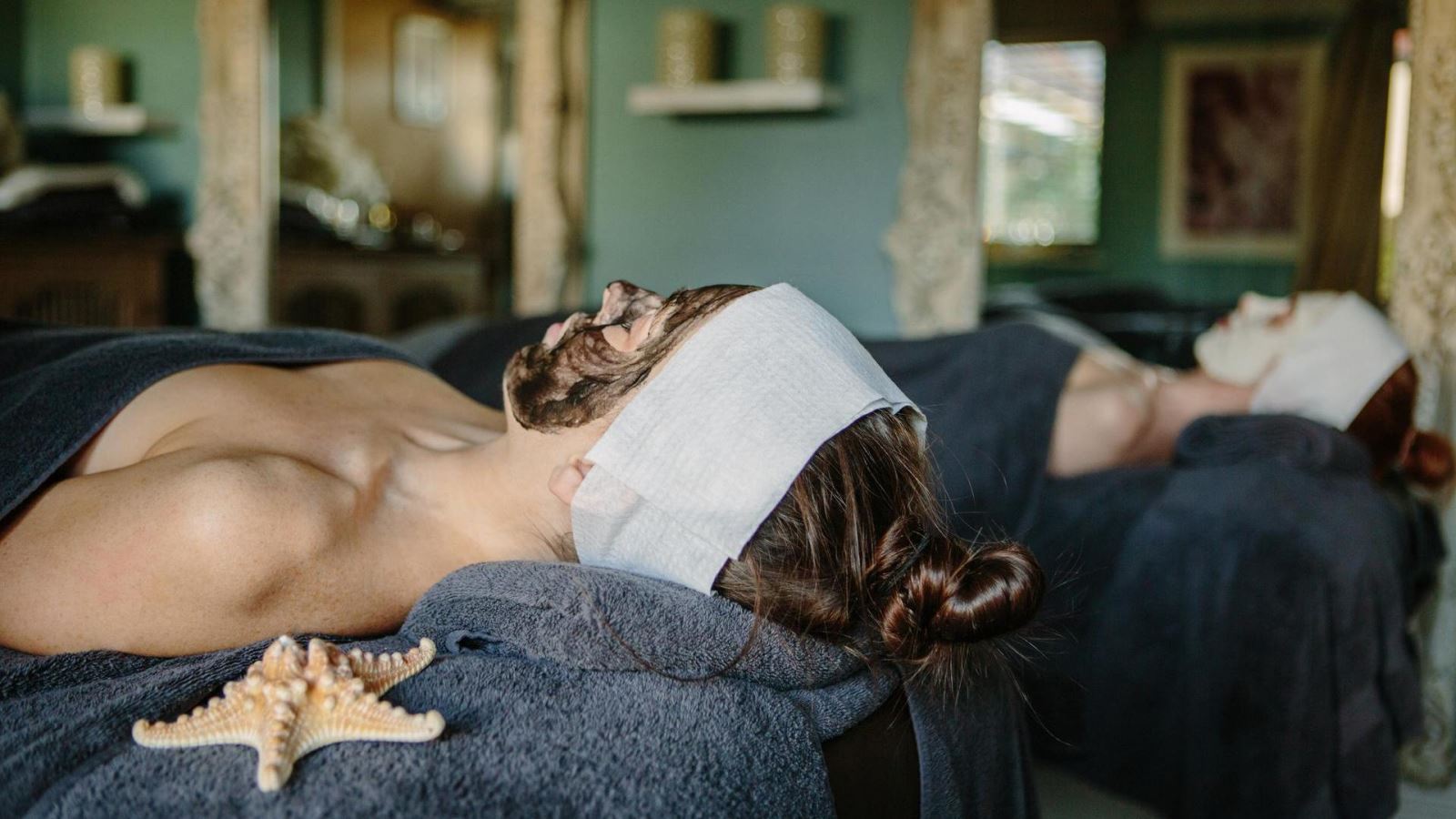 Two women laying down on spa beds underneath towels with a face mask on at Roslin Beach Hotel Spa